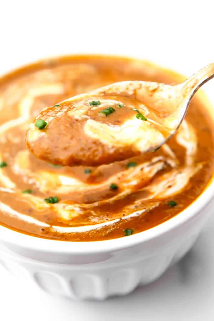 A white bowl filled with pumpkin bean soup with a spoonful above it.