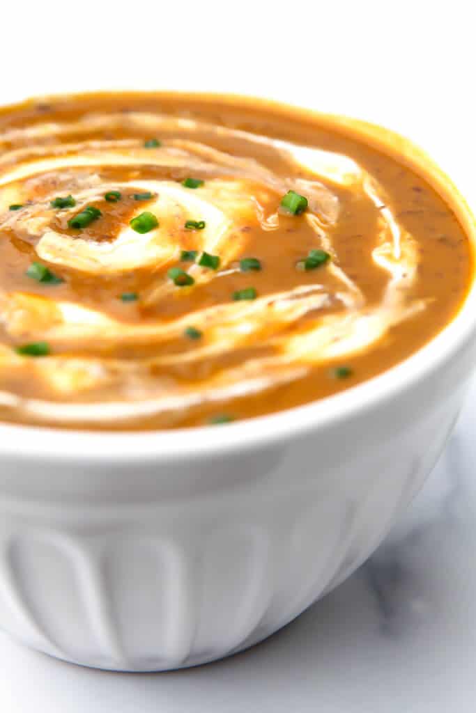 A bowl of bean soup pureed with pumpkin and topped with a swirl of sour cream in a white bowl.
