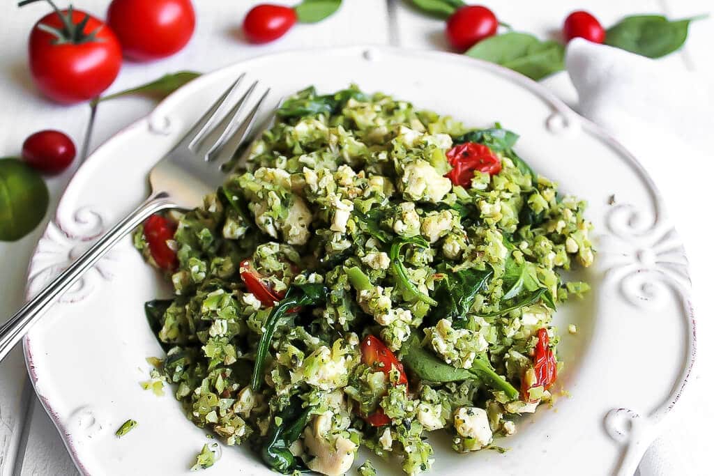 A plate of pesto and veggie tofu scramble made with veggies and pesto with tomatoes behind it.