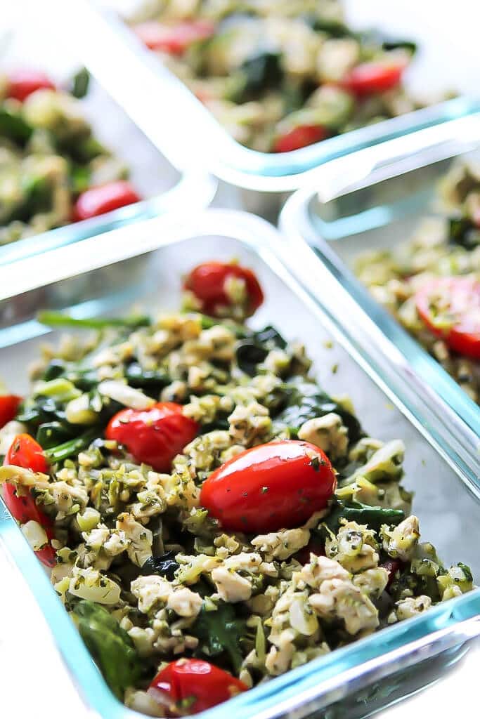 Containers of vegan tofu scramble with pesto spinach, broccoli, and tomatoes packed for grab and go breakfasts.