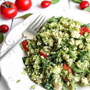 A white plate full of veggie packed vegan tofu scramble made with broccoli, zucchini, spinach, and cherry tomatoes.