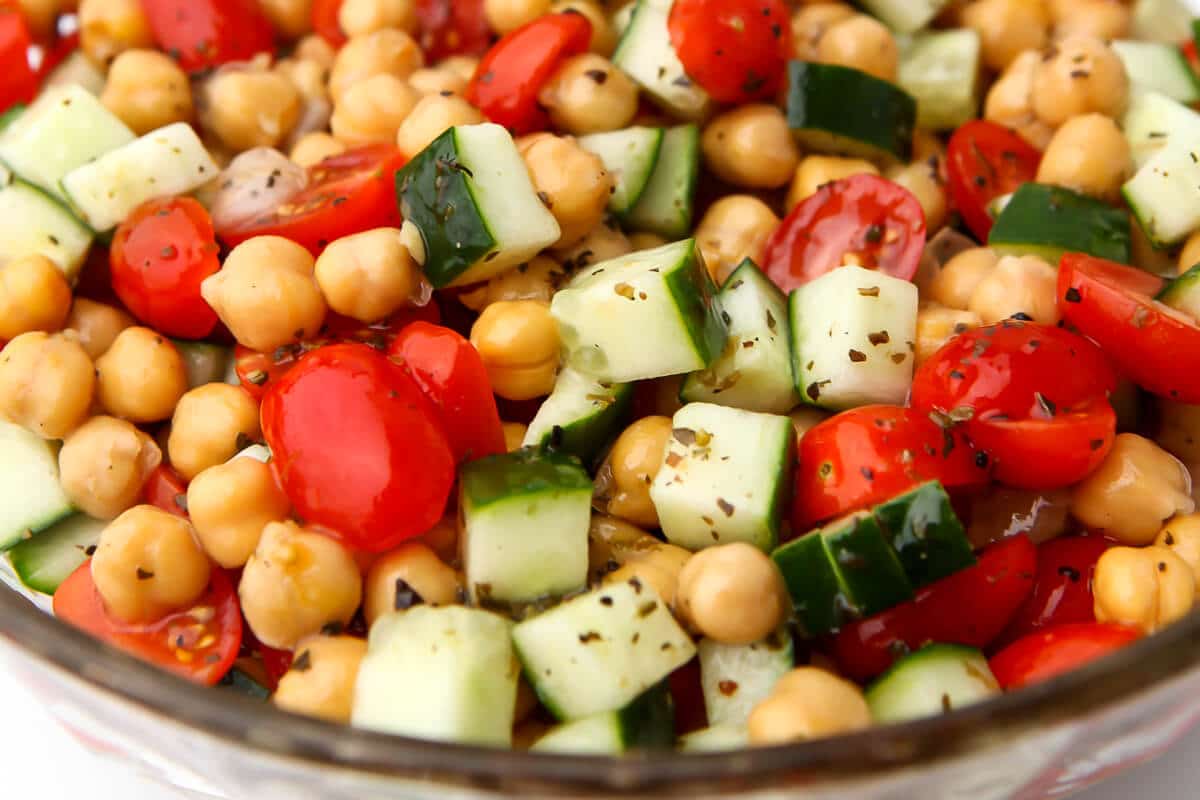 A glass bowl filled with a vegan chickpea salad with colorful tomatoes and cucumbers.