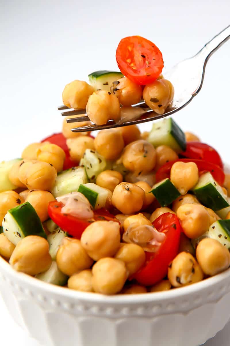 A fork full of chickpea salad over a white bowl filled with the salad.