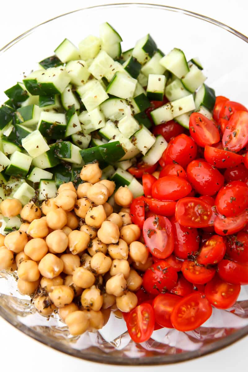 A bowl with chickpeas, sliced cherry tomatoes, and diced cucumbers before mixing the chickpea salad.