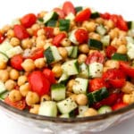 A glass bowl filled with vegan chickpea salad with tomatoes and cucumbers.
