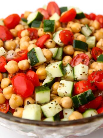 A glass bowl filled with vegan chickpea salad with tomatoes and cucumbers.