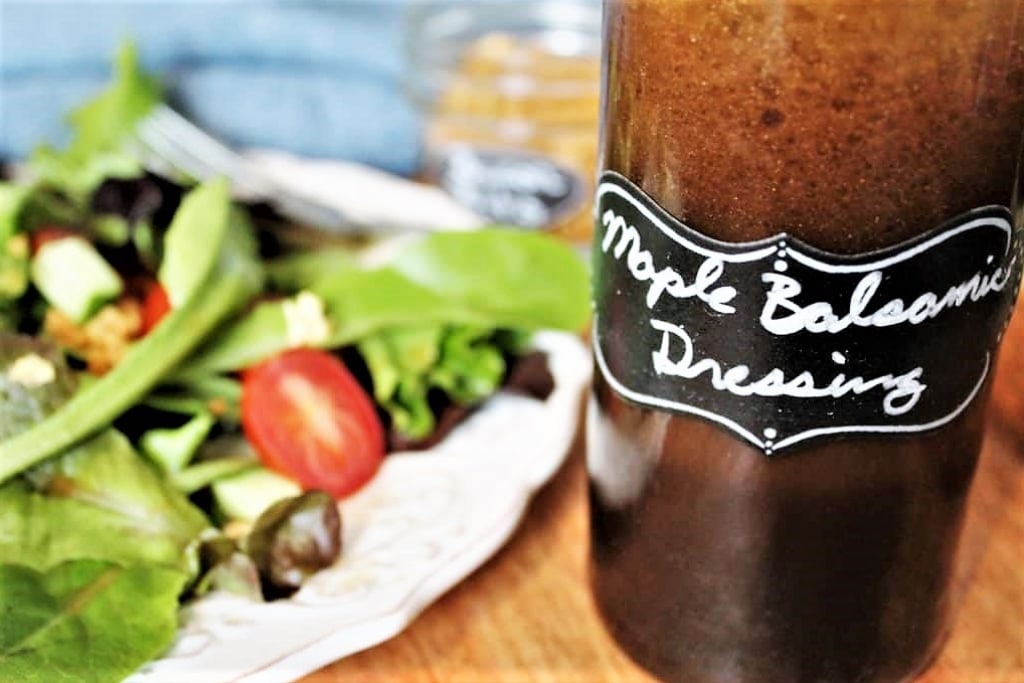 A bottle of maple balsamic dressing with a salad in the background.