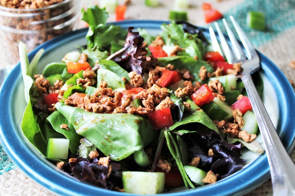 A salad with maple balsamic vinaigrette dressing and bacon bits , red peppers, and cucumber.