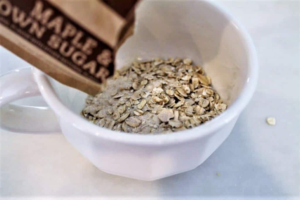 Instant oatmeal being poured into a mug to make a mug muffin.