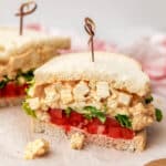 A tofu egg salad sandwich with sliced tomatoes and lettuce on white bread.