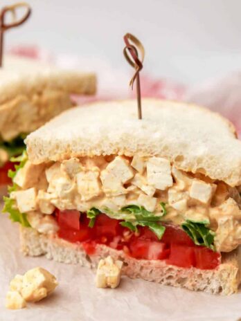 A tofu egg salad sandwich with sliced tomatoes and lettuce on white bread.