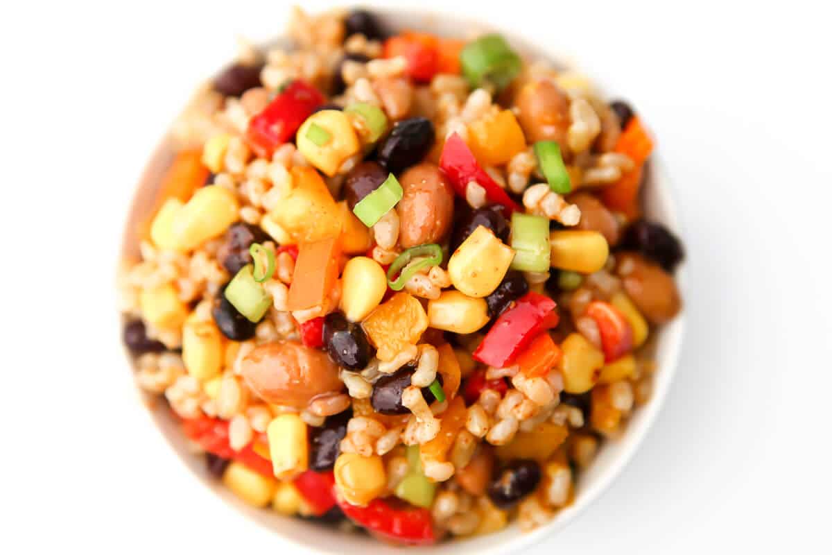 A close up top view of a bowl of vegan bean salad with beans, rice, chopped bell peppers, and green onions.