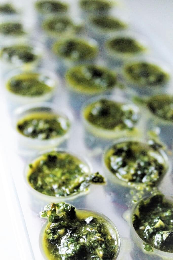 A silicone ice cube tray filled with pesto ready to freeze into cubes.