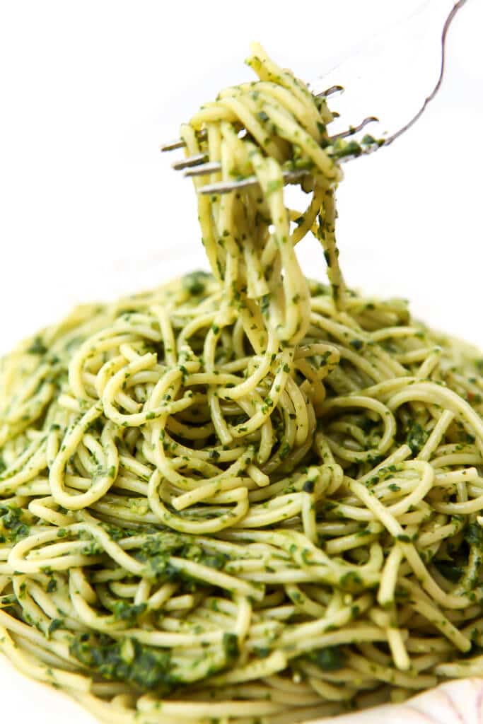 Noodles covered in vegan pesto with a fork lifting up some noodles.