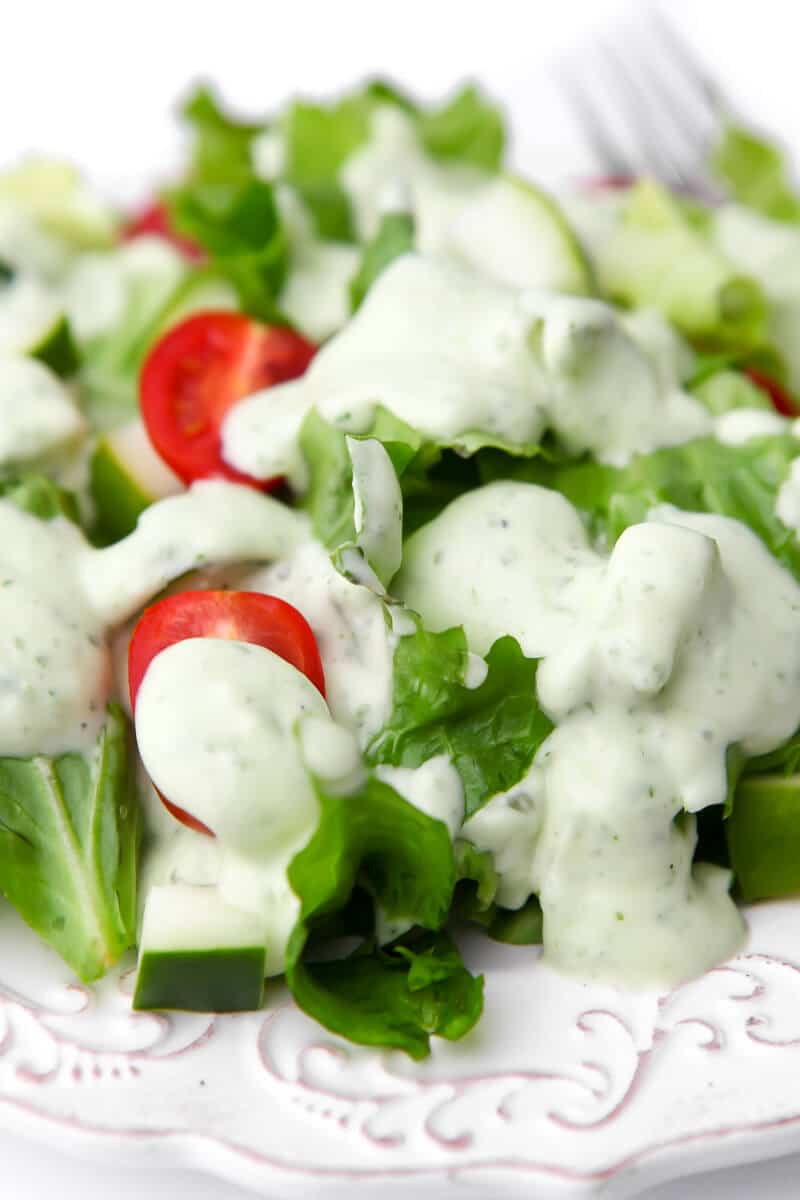 A close up of a salad with rich and creamy vegan ranch and tomatoes on it.