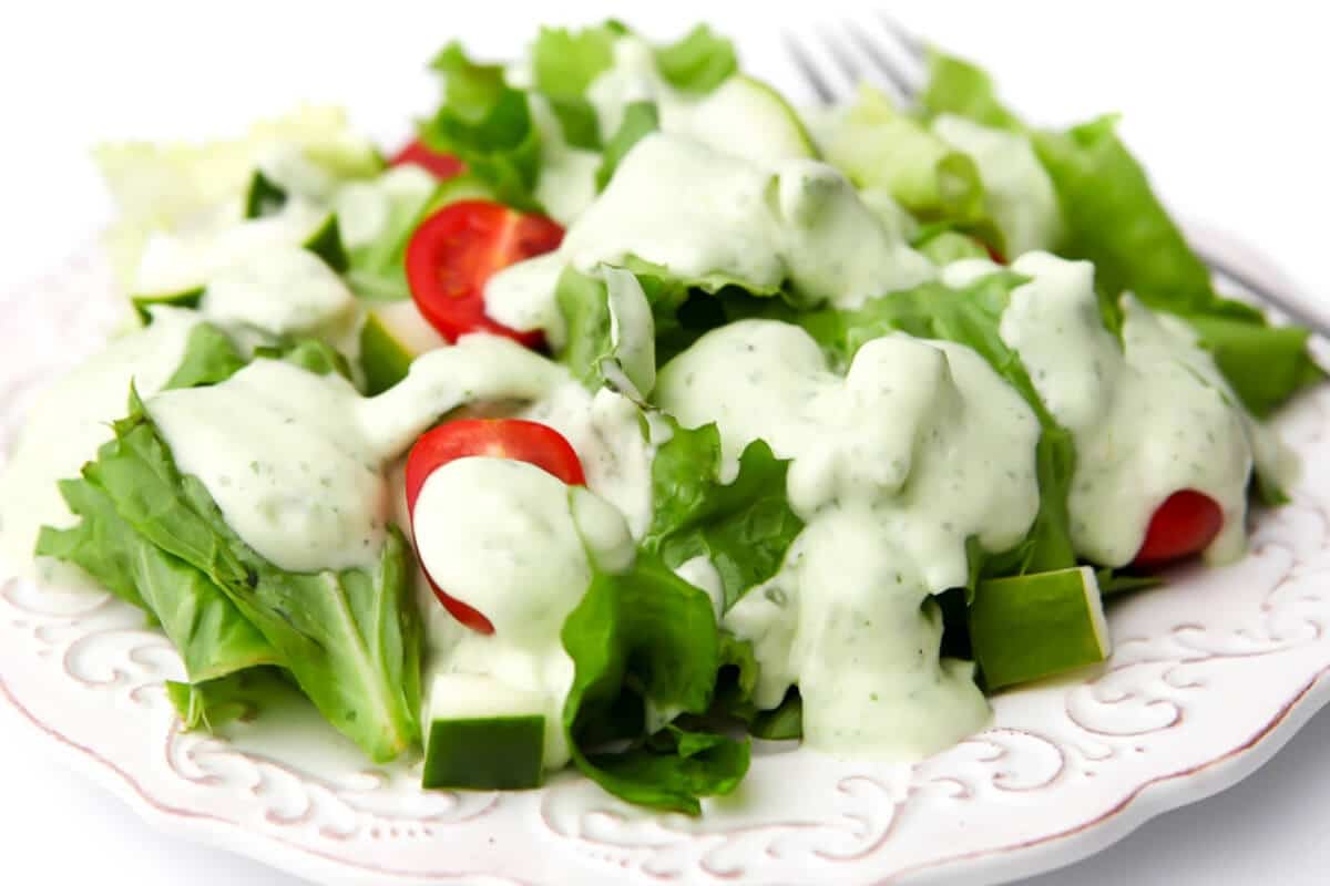 A plate filled with lettuce and tomatoes with vegan ranch dressing drizzled over it.