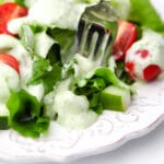 A white plate filled with salad drizzled with vegan ranch dressing with a fork sticking in it.