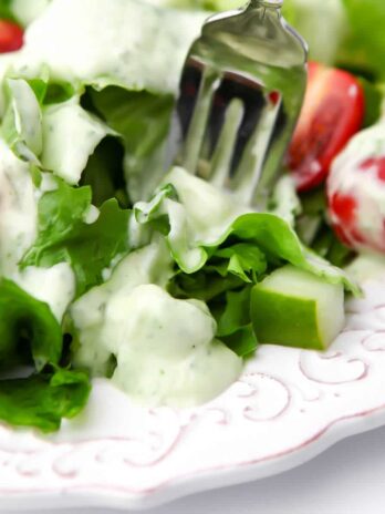 A white plate filled with salad drizzled with vegan ranch dressing with a fork sticking in it.