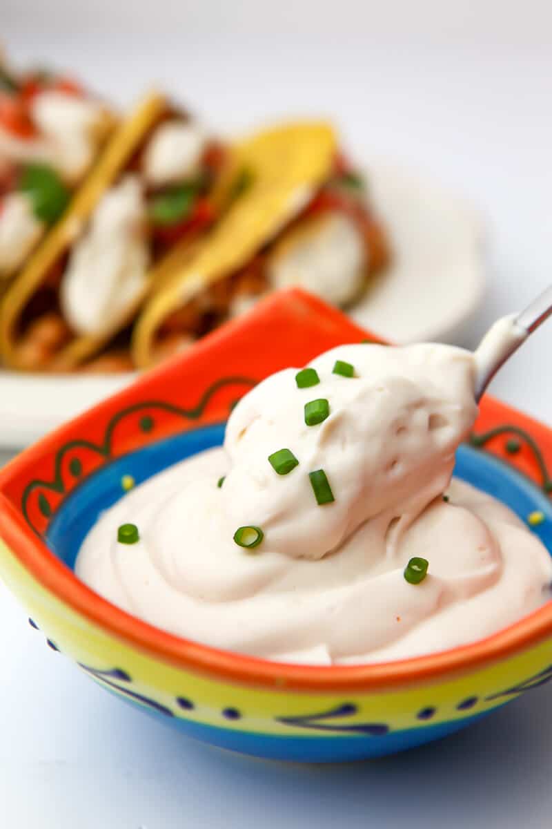 Thick and creamy vegan sour cream being spooned out of a colorful bowl.