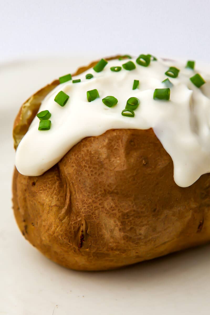 A baked potato with vegan sour cream and chives on top.