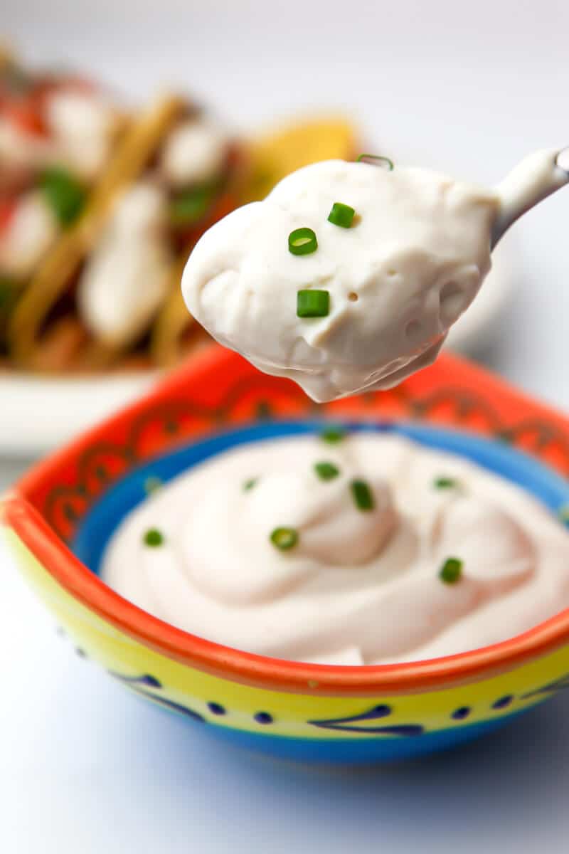 A colorful little bowl filled with homemade vegan sour cream with a spoonful over it.