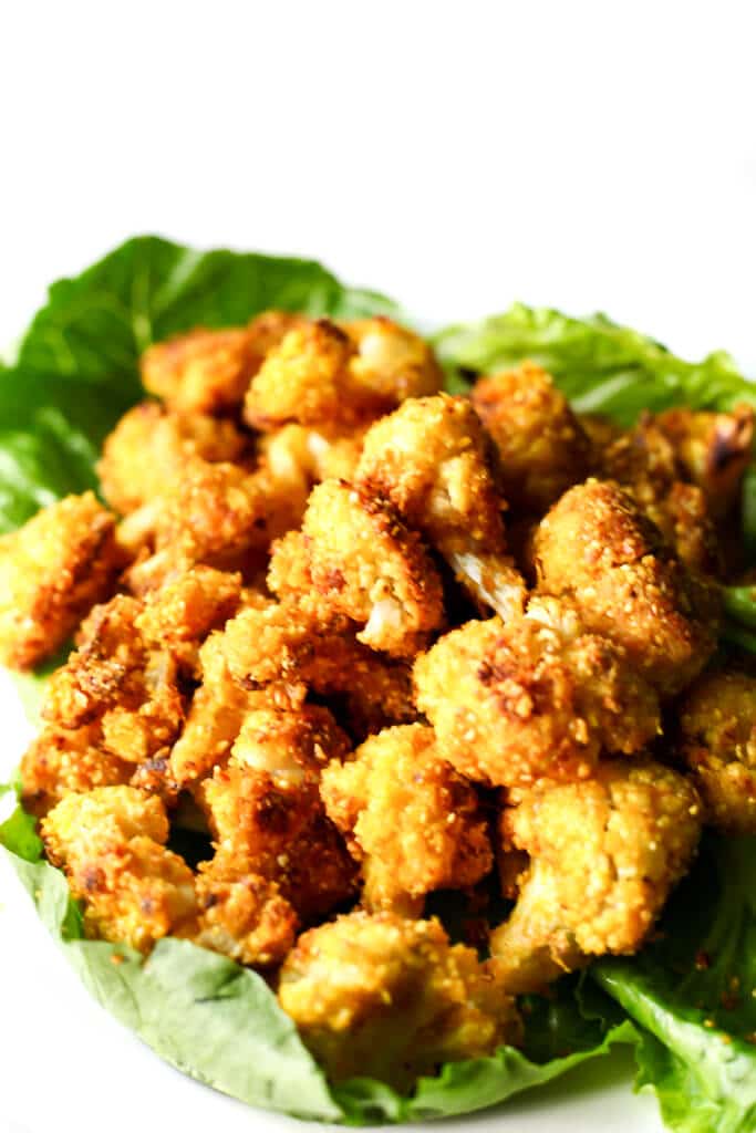 A plate with a bed of lettuce and roasted cauliflower nuggets on top.