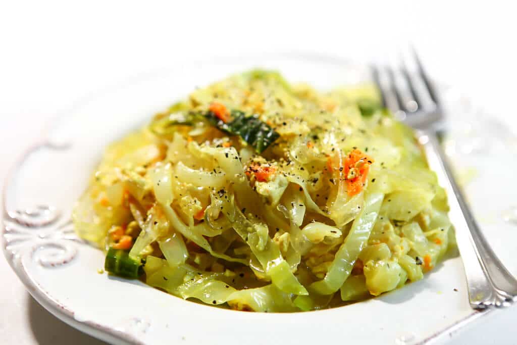 A white plate with vegan Haluski made with cabbage and noodles with a fork on the side.