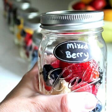 A mason jar smoothie ready to be blended with more make-ahead smoothies behind it.