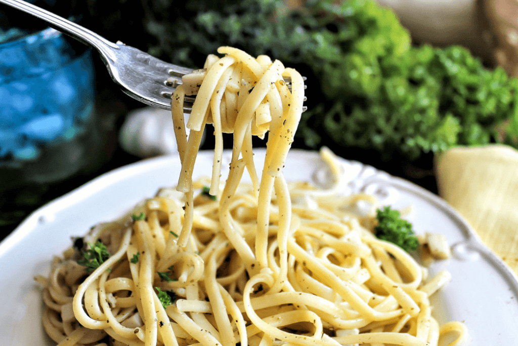 A fork loaded with vegan linguine with clam sauce over a plate full of the pasta.