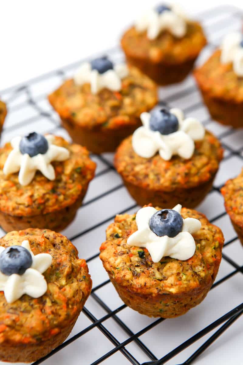 A top view of zucchini carrot muffins with a dollop of frosting and a blueberry on top.