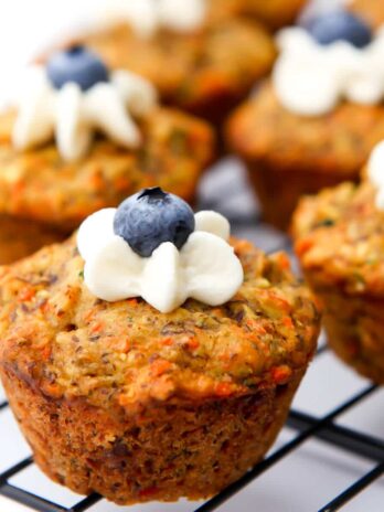 A close up of healthy vegan muffins with a dollop of frosting and a blueberry on top.