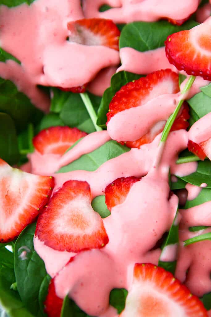 A close up of baby spinach with sliced strawberries and pink strawberry dressing over it.