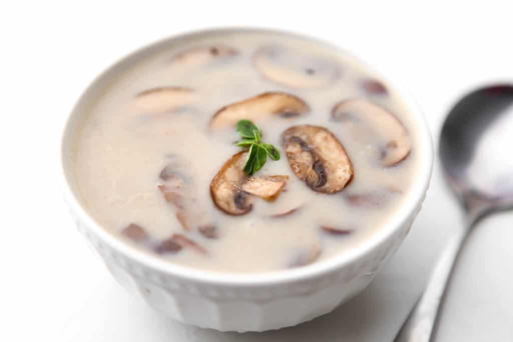 A white bowl filled with dairy-free cream of mushroom soup with a spoon on the side.