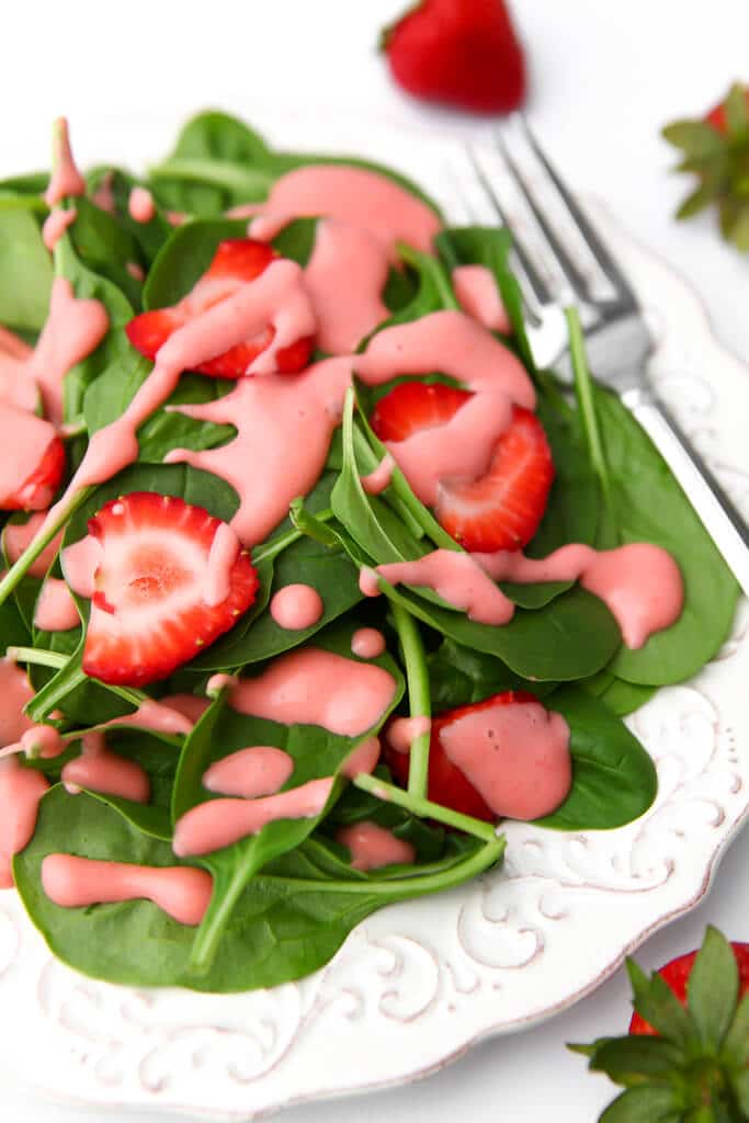 A vegan strawberry spinach salad on a white plate with strawberries on top and around the plate.