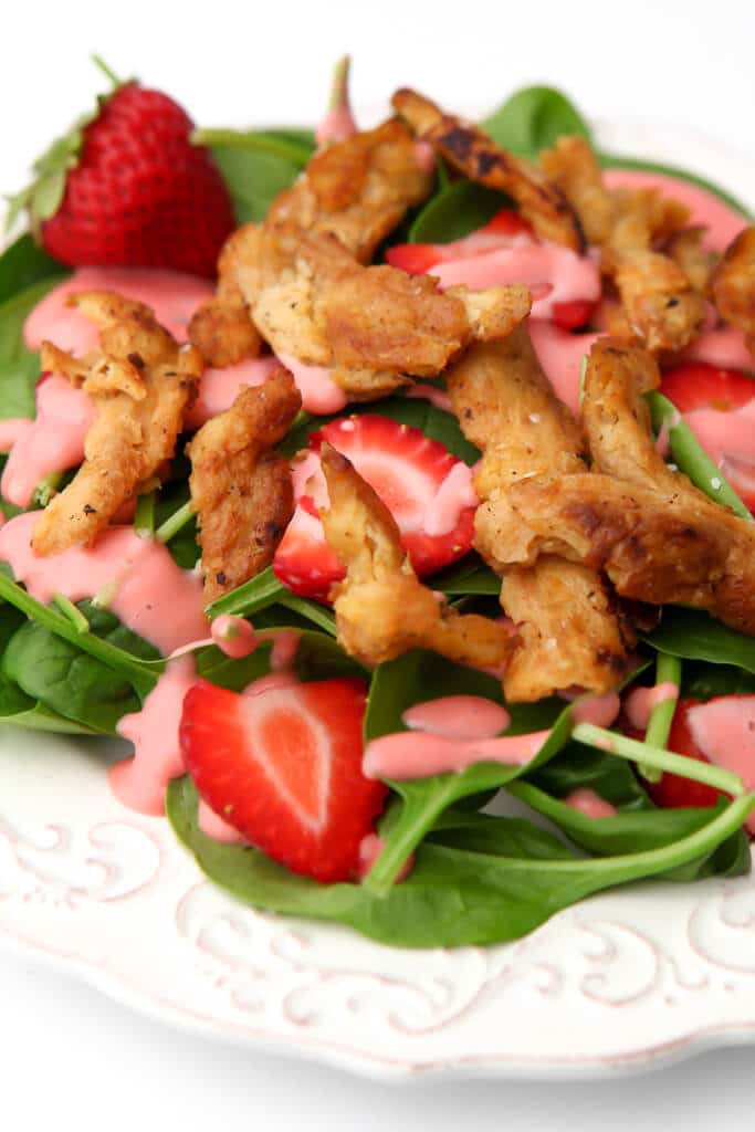 A strawberry and spinach salad with strawberry dressing and vegan chicken strips on top.