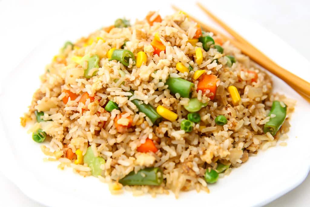 A white plate of vegan fried rice with chop sticks on the side.