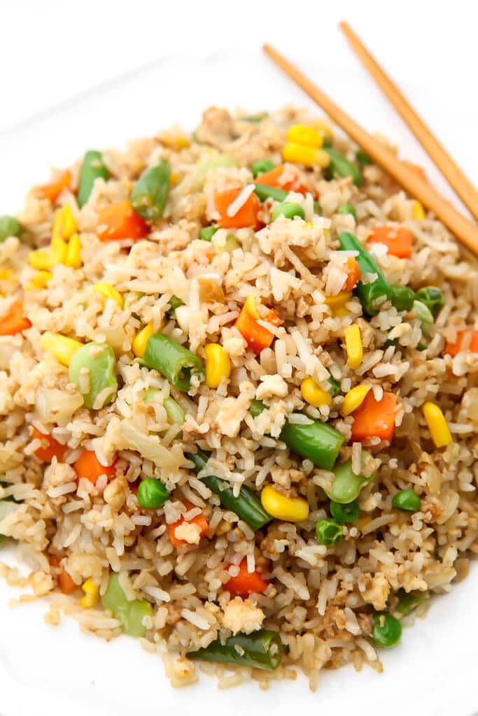 A white plate filled with vegan fried rice made with mixed veggies and tofu with chop sticks on the side.