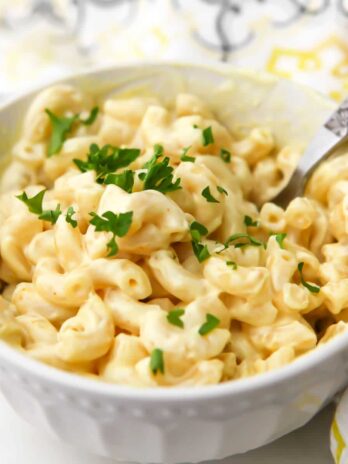 A bowl of easy vegan mac and cheese with parsley on top and a fork in it.