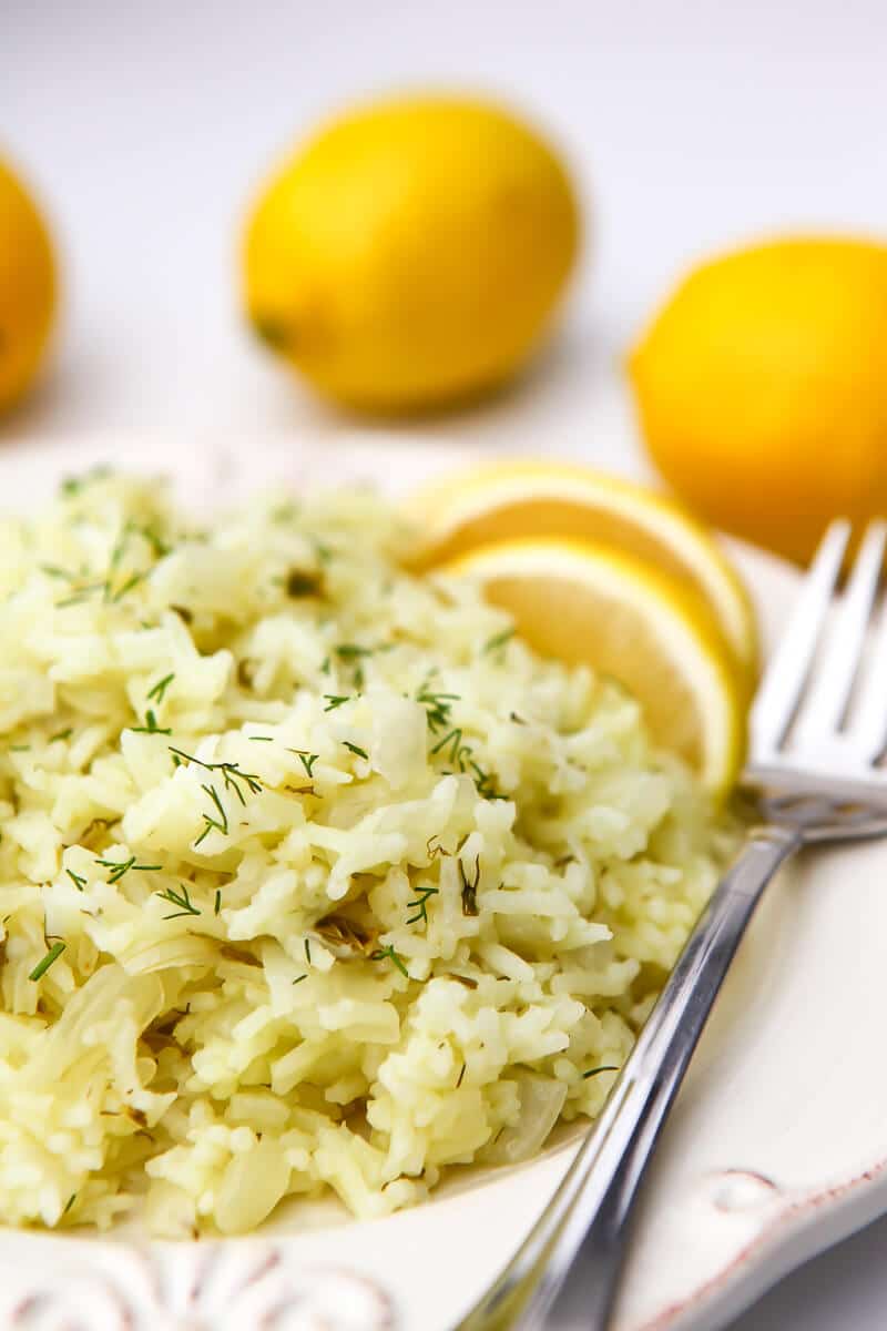 A white plate with lemon rice on it with 3 lemons in the background.