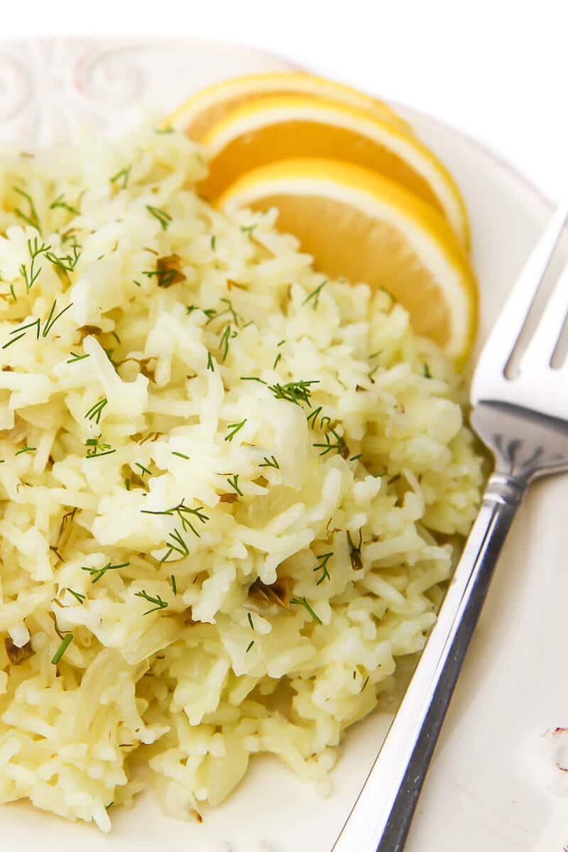 A close up of a white plate filled with herbed lemony rice with lemon wedges on the side.