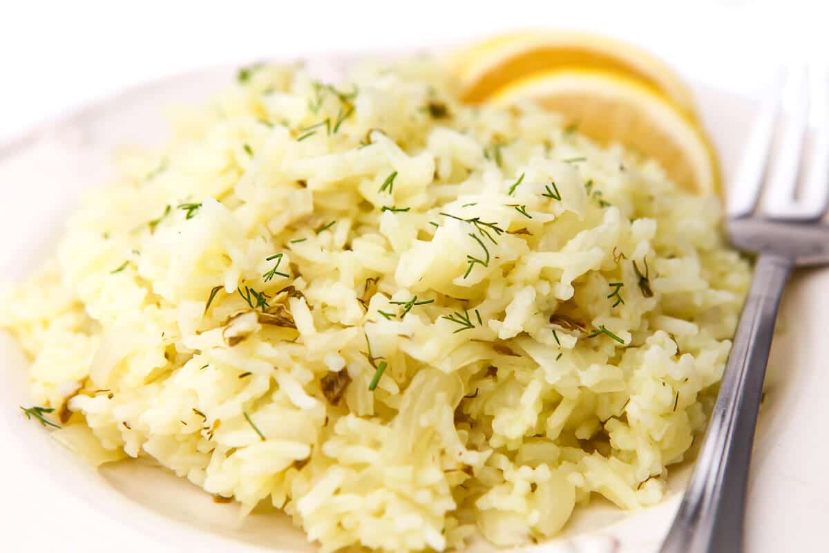 A plate full of lemony rice with mint and dill in it and lemon wedges on the side.