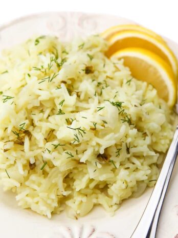 A white plate filled with lemon rice with wedges of lemons and a fork on the side.