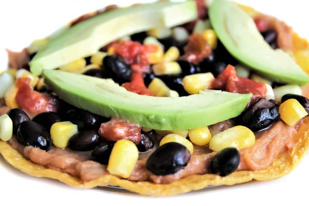 A gluten free vegan tostada top with re-fried beans, black beans, corn, and avocado. 