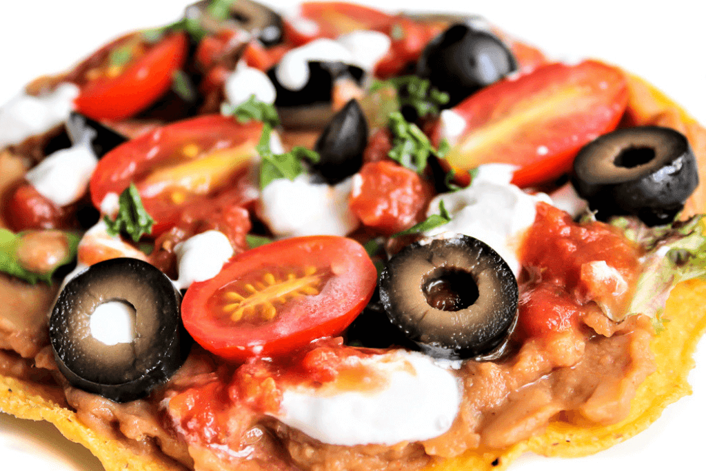 a tosada shell with cheese, olives, and tomatoes.