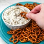 A white bowl filled with vegan clam dip on a blue plate with pretzels on it.