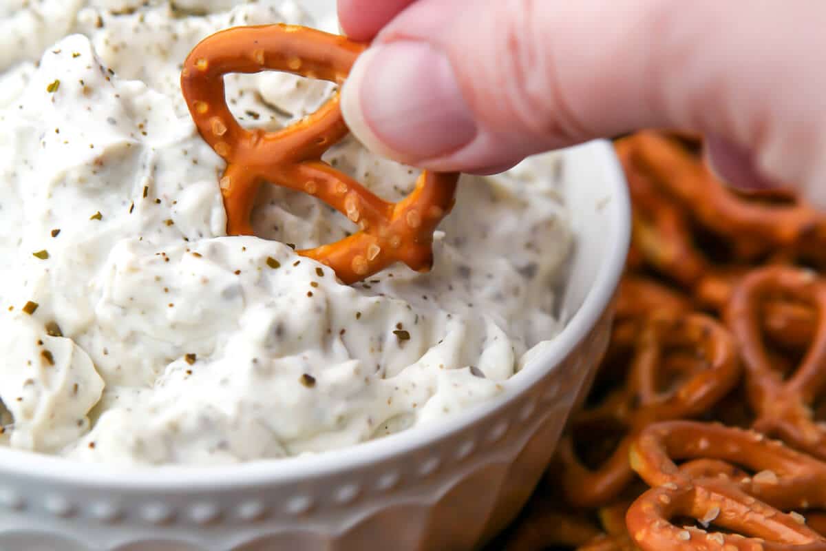 A close up of vegan clam dip being scooped with a pretzel.