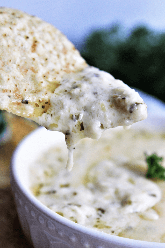 A white bowl filled with easy to make artichoke dip with a chip dipped into it.