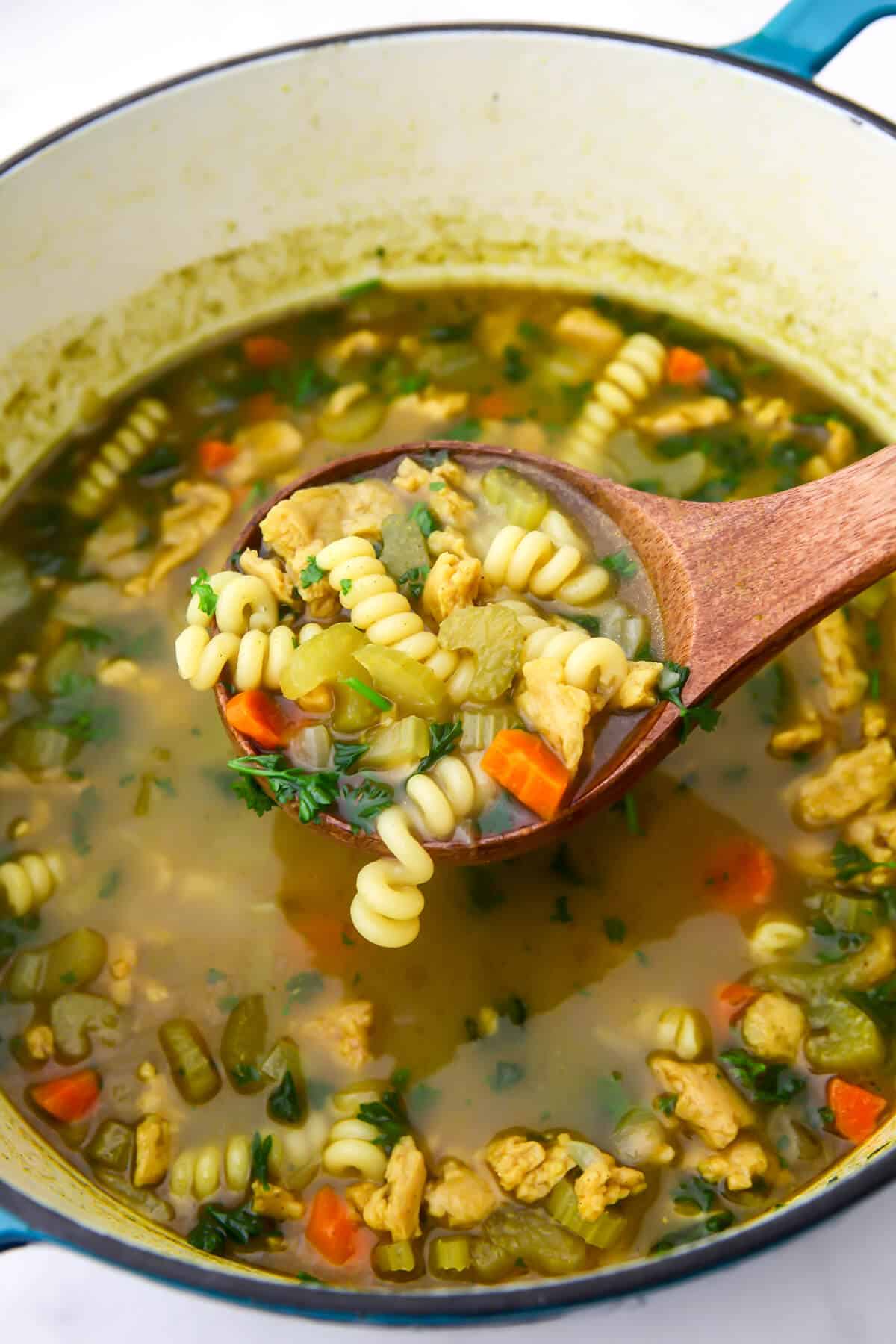 A large pot filled with vegan chicken noodle soup with carrots, celery, and soy curls in it.