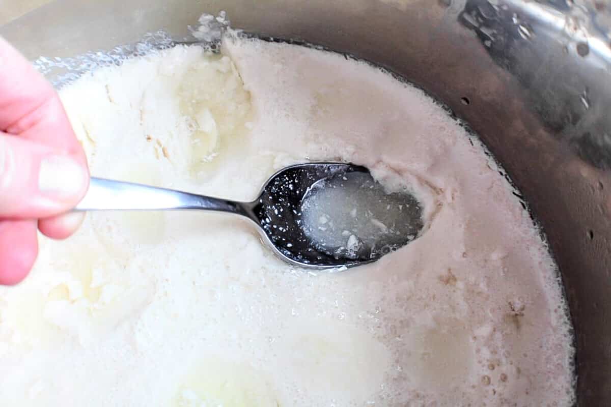 A spoon scooping up water off the top of soy yogurt in an Instant Pot.