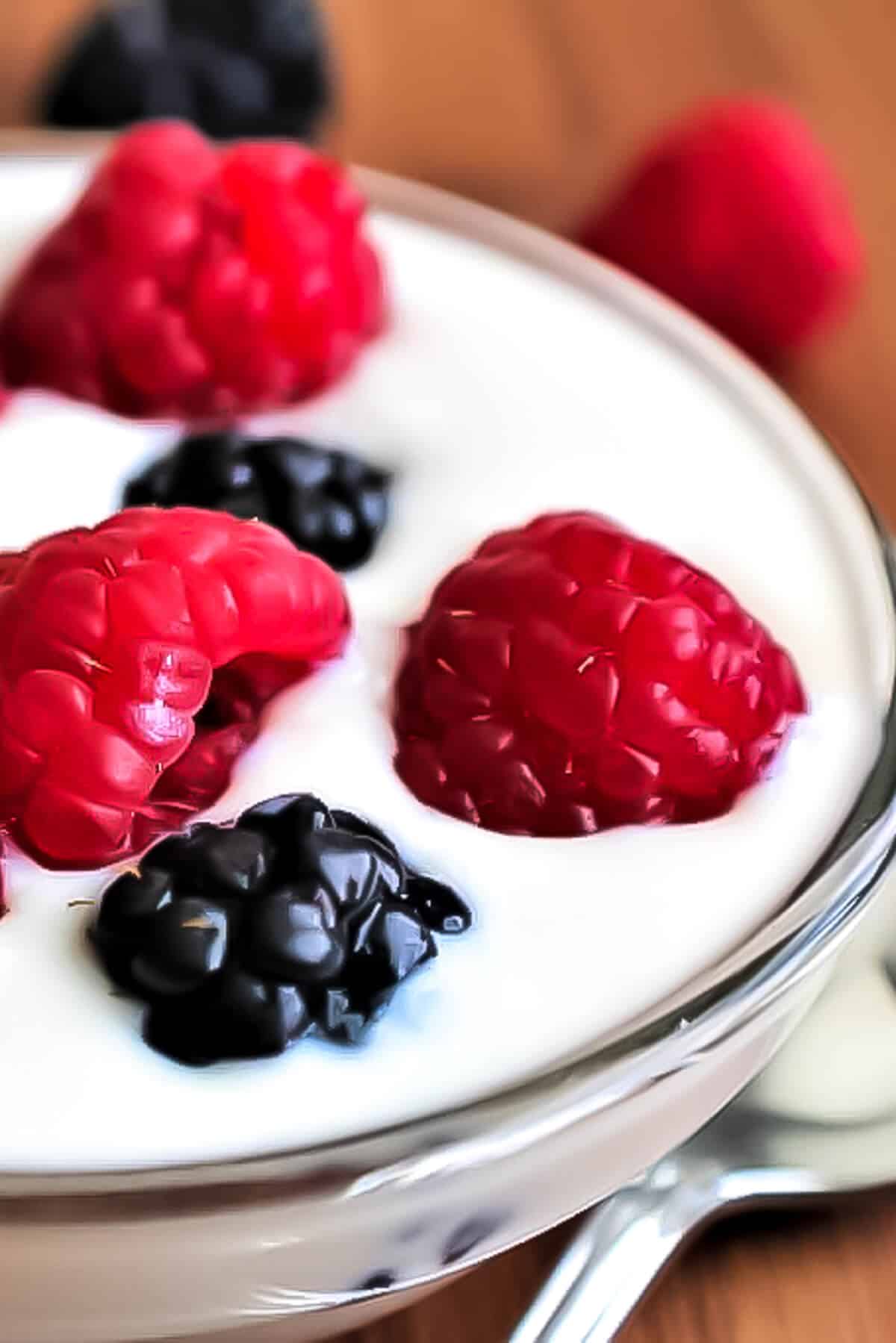 A bowl of vegan yogurt with berries on top and a spoon beside it.